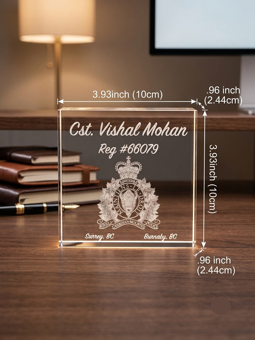 Clear glass plaque with engraved text and logo on a wooden surface, with measurements indicated.